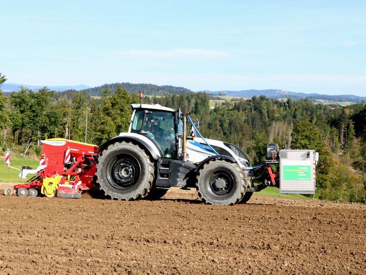 Ein Traktor fährt mit Sämaschine und Messgerät auf Acker.