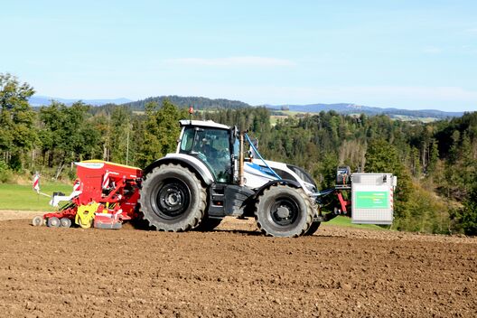 Ein Traktor fährt mit Sämaschine und Messgerät auf Acker.